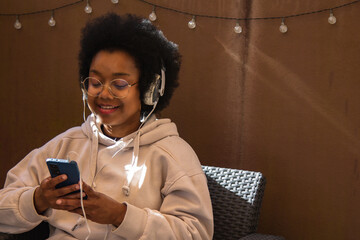 African American woman relaxing on the terrace of her house listening to music with headphones