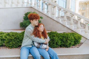 Redhead boy hugging redhead girl outdoors on stone bench near building