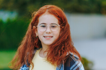 Redhead girl with glasses smiling confidently at camera outdoors in casual style