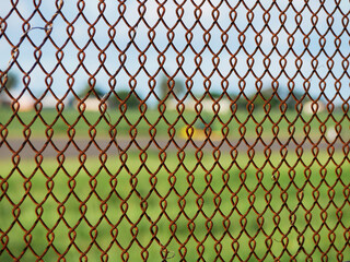 Fototapeta premium rusty iron fence with green meadow, a runway and white houses in the background