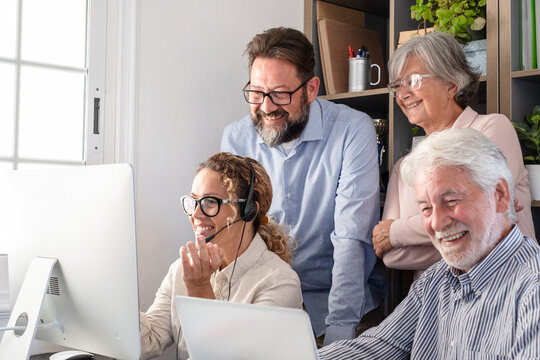 Group of mature and senior professionals working together in a modern office. Men and women collaborate around a computer discussing ideas and reviewing information. Teamwork, mentoring, cooperation