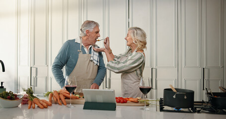Cooking, taste and senior couple in kitchen for lunch, online recipe and prepare food for bonding in home. Tablet, retirement and old man and woman for meal prep, wine and help for anniversary dinner
