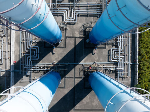 Industrial gas facility with blue towers, pipes, and power lines in rural area. - Powered by Adobe