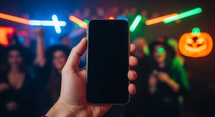 Close-up of a hand holding a smartphone with a blank screen at a vibrant Halloween nightclub party with colorful neon lights.