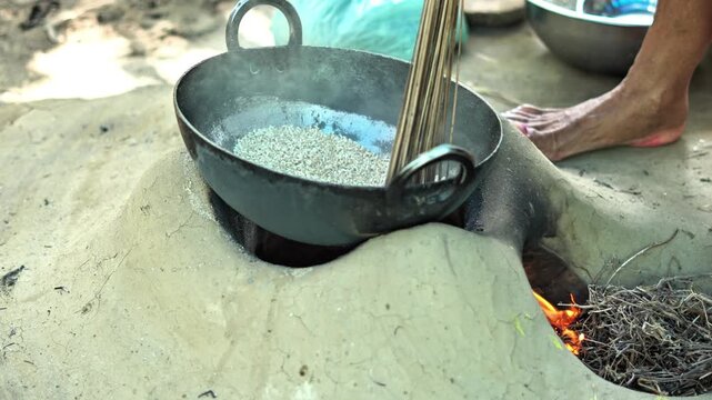 An Indian women make puffed rice on mud stove. Indian village landscape.