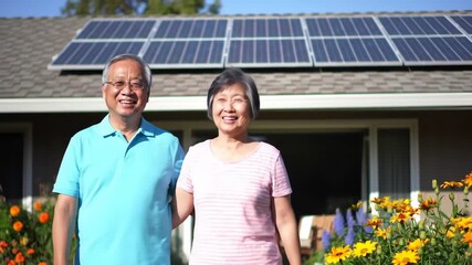 Smiling Asian couple in front of house with solar panels, advertising renewable energy - Powered by Adobe