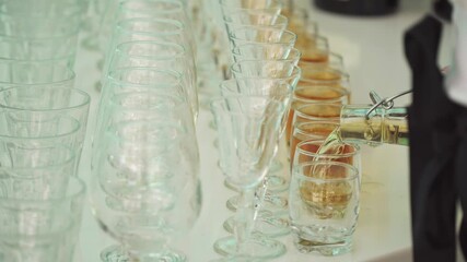 The waiter pours alcohol into glasses on the white table