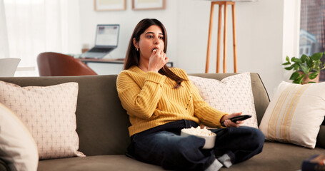 Eating, popcorn and woman with remote, home and watching tv with app subscription and entertainment. Indian person, relax and streaming movies on website, online and chilling with snack on couch