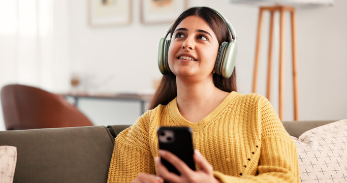 Thinking, headphones and woman with phone in home, streaming podcast or listening to music. Smile, mobile and person with idea for audio on sofa in living room, online radio and playlist decision - Powered by Adobe