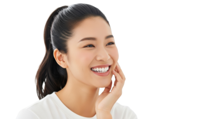 Young East Asian woman with dark ponytail, white top, smiling broadly with bright white teeth, hand to cheek, against soft white bokeh background. Concept of radiant health and well-being