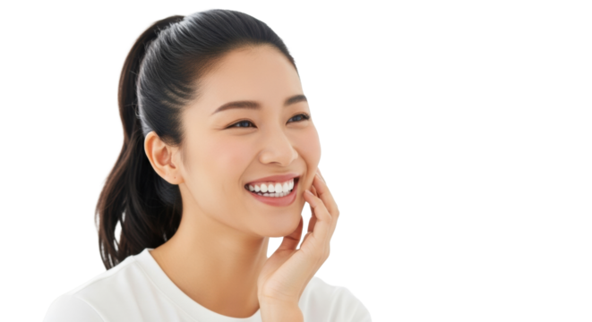 Young East Asian woman with dark ponytail, white top, smiling broadly with bright white teeth, hand to cheek, against soft white bokeh background. Concept of radiant health and well-being