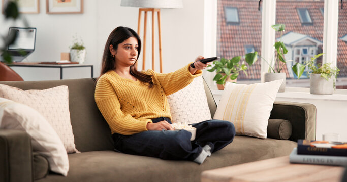 Home, relax and woman with remote, watching tv and streaming movies with subscription in living room. Channel, change and Indian person with control for entertainment, chill or comfortable on sofa