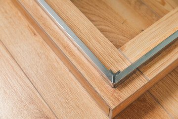 Shower stall threshold. The floor is made of wood-look tile and the shower is enclosed in glass. The edge of the shower stall has a thin, silver trim. Glass door hinges.