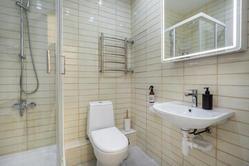 This neat bathroom features a glass shower, a wall-mounted toilet, and a small sink. The light-colored tiles and fixtures create a bright, clean atmosphere, perfect for relaxation