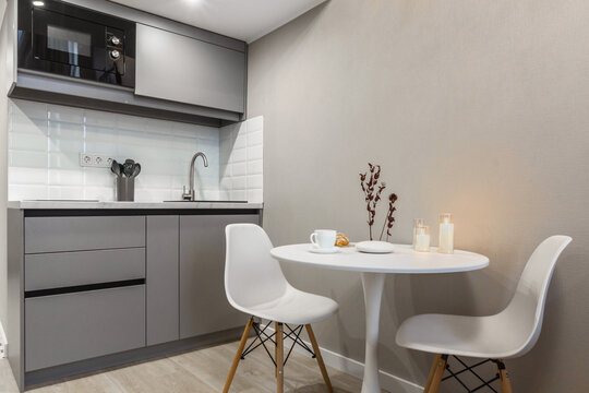 A modern kitchen corner features a round white table and two chairs, with a small vase on the table. The sleek gray cabinets and appliances create a calm atmosphere perfect for enjoying meals