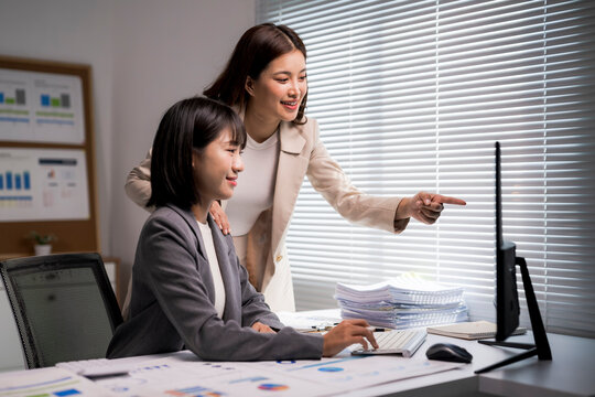 Asian businesswomen collaborating, discussing data on computer at office