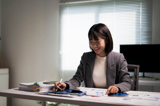 Asian businesswoman smiling while analyzing financial data at office desk