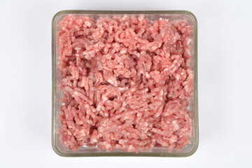 An overhead shot of a square glass dish completely filled with raw, light pink ground pork, centered on a plain white background