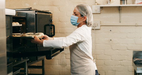 Bakery, woman and bread in oven in kitchen for breakfast order, baking process or catering service. Hospitality industry, baker or mask in small business for lunch roll preparation or culinary skills