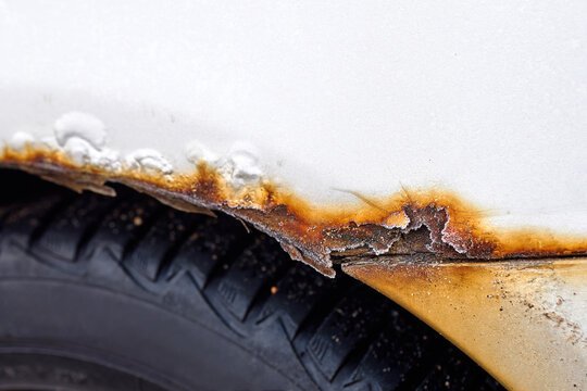 Car rear wheel area with visible rust corrosion and salt damage on fender, effect of poor maintenance during winter season. Closeup of rusted metal fender showing corrosion, oxidation, and decay