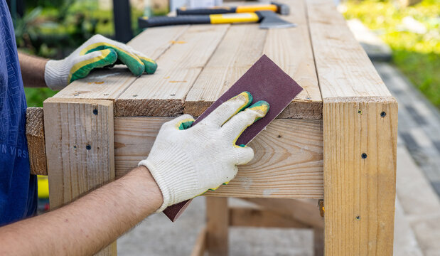 Tools for sanding wood. Carpenter sanding wooden plank on table, closeup. Sanding wood with sandpaper.
