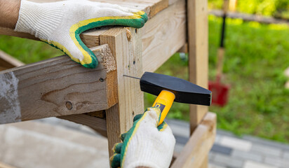 Close-up. Carpenter with hammer and nails fixes a wooden board. Construction industry, do it...