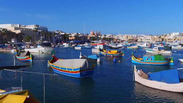 Aerial view of Marsaxlokk harbor in Malta with luzzu boats, domed parish church, and waterfront. Boats bob and lines ripple on a sunny day with crisp color.