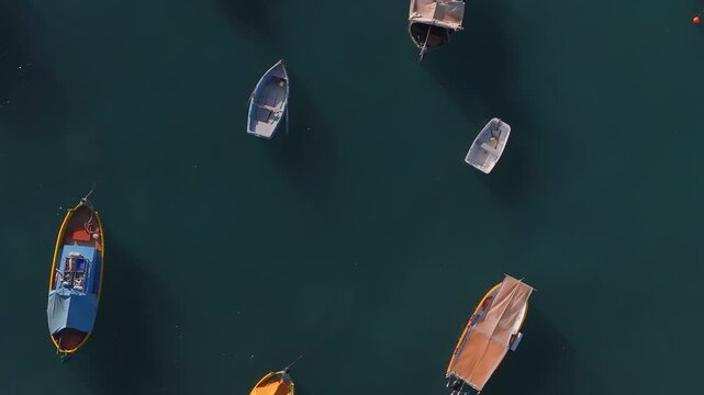 Aerial top down view of Maltese luzzus and dinghies in Marsaxlokk harbour, Malta. Boats bob and rotate near buoys and lines, soft low angle light, long shadows.
