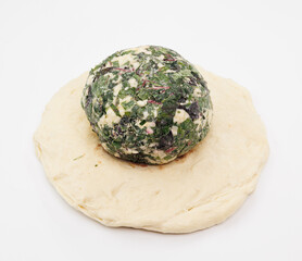 A spinach and cheese mixture formed into a sphere rests on a round dough disk, suggesting a fresh Pkhlovana Khachapuri ready for baking.