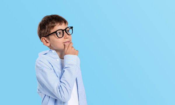 Thoughtful kid boy in glasses touching chin with hand while thin