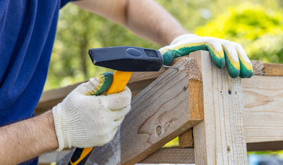 Hand holding a hammer to drive nails into the wood. Carpenter with hammer and nails fixes a wooden board. Construction industry, do it yourself. Wooden work table. Close-up.