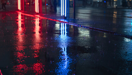Wet street at night with red and blue light reflections.
