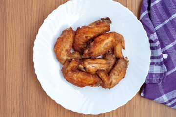 A top-down view of several golden-brown fried chicken wings, a popular protein-rich food, served on a white plate. A purple napkin sits on the wooden table.