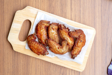 A top-down, high-angle view of six crispy fried chicken wings, a protein-rich food, served on white parchment paper on a wooden cutting board.