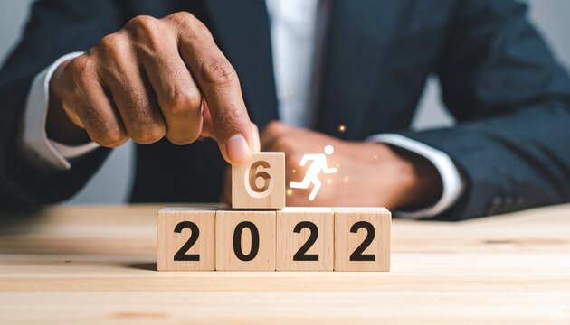 Business hand placing milestone block with running figure on 2022 stack.