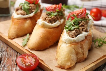 Delicious bruschettas with tuna, cream cheese and tomatoes on wooden table, closeup