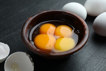 Raw eggs and yolks on black table, closeup
