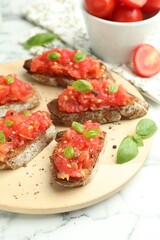Tasty bruschettas with tomatoes and basil on white marble table, closeup