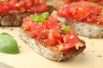 Tasty bruschettas with tomatoes and basil on wooden board, closeup