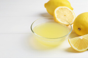 Lemon juice in glass and fresh lemons on white wooden table, closeup. Space for text
