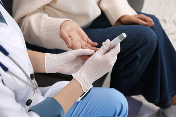 Fototapeta premium Diabetes. Doctor in medical gloves checking patient's blood sugar level with lancet pen indoors, closeup