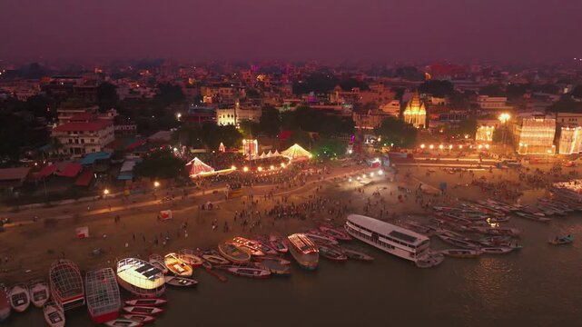 Cinematic drone shot of morning Ganga Aarti at Assi Ghat, Banaras. Priests perform sacred rituals with lamps while the Ganga River glows with soft sunrise reflections and peaceful boats.