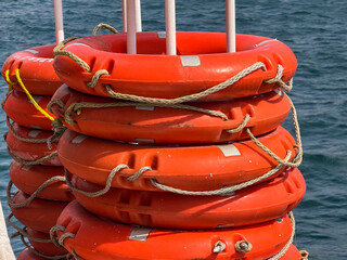 Stacked orange lifebuoys tied with ropes on the deck of a passenger yacht. Maritime safety detail during sea transportation across the sea.