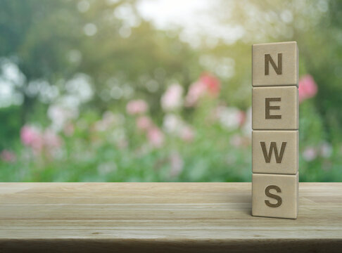 NEWS letter on wood block cubes on wooden table over blur pink flower and tree in park, Business communication concept