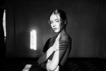 A black-and-white photograph of a woman posing contemplatively against a dark background with dramatic lighting.