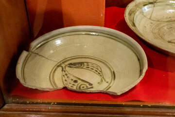 Old ceramic bowl with hand-painted fish motif from Thailand, displayed in a museum. Traditional antique pottery showing ancient craftsmanship and cultural heritage.