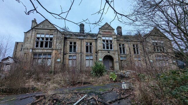 Derelict Old Batley General Hospital, vandalised District Cottage Medical Centre. Abandoned country mansion grounds in disrepair. Boarded up, imposing, creepy, empty haunted building through branches.