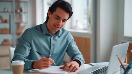 Focused businessman diligently writing at his desk with a laptop and coffee. The setting is bright and professional, suggesting a productive workspace Stock Video - Powered by Adobe