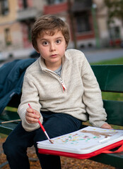 Portrait of a 7-year-old boy drawing in the park on an autumn day