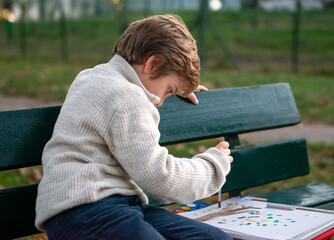 Portrait of a 7-year-old boy drawing in the park on an autumn day